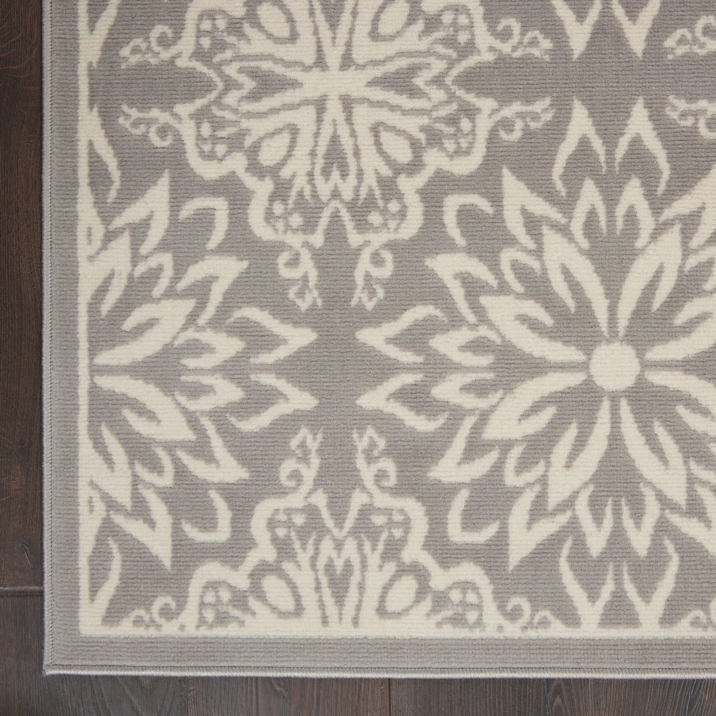 Gray and ivory damask floral area rug on wood floor; rectangular with pale border and bold blossom motifs