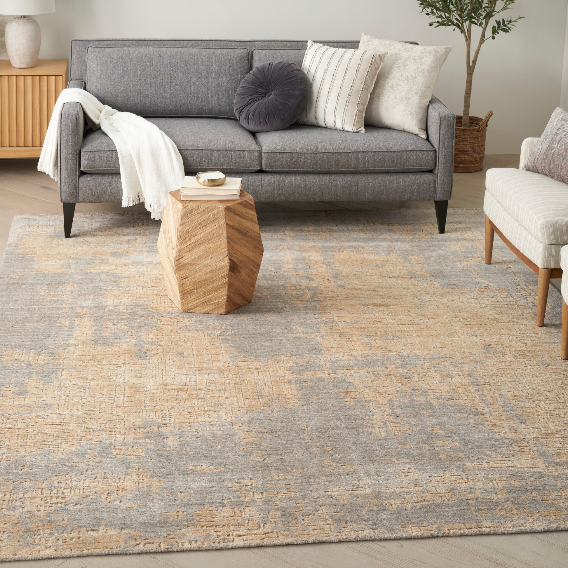 Gray fabric sofa with cushions and white throw, modern living room on a beige textured rug with a geometric wooden side table.