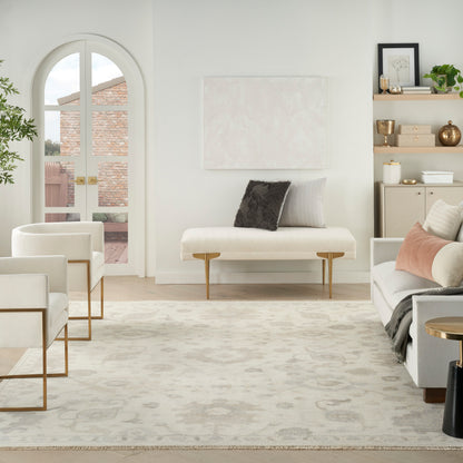 Bright modern living room with white upholstery, light wood legs, gold metal accents, beige rug, abstract wall art, and an arched window.