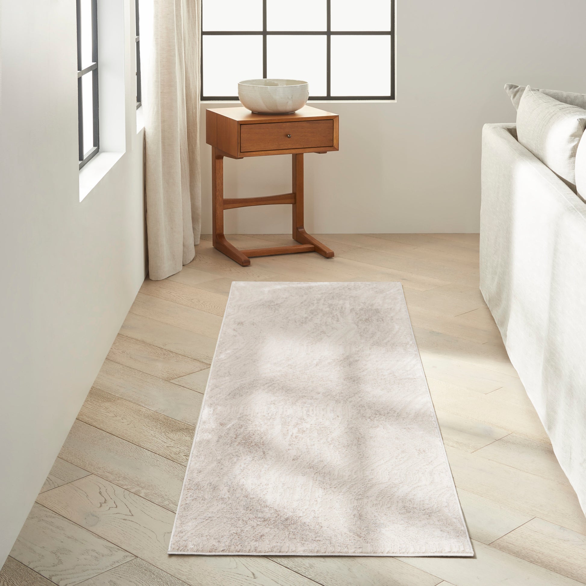 Light beige runner rug on pale wood floor beside sofa; wooden side table with ceramic bowl near window.