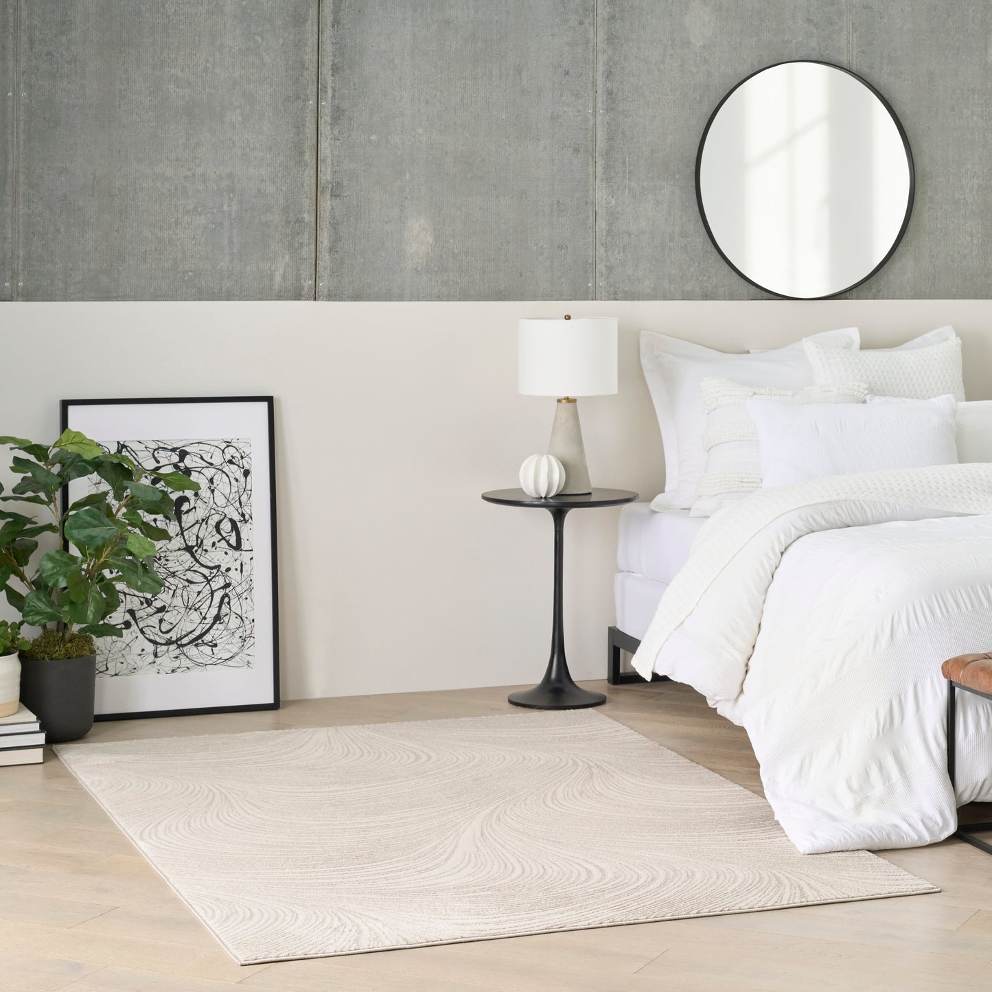 Beige woven area rug in a modern bedroom beside a white bed, with a round wall mirror, black side table, and plant.