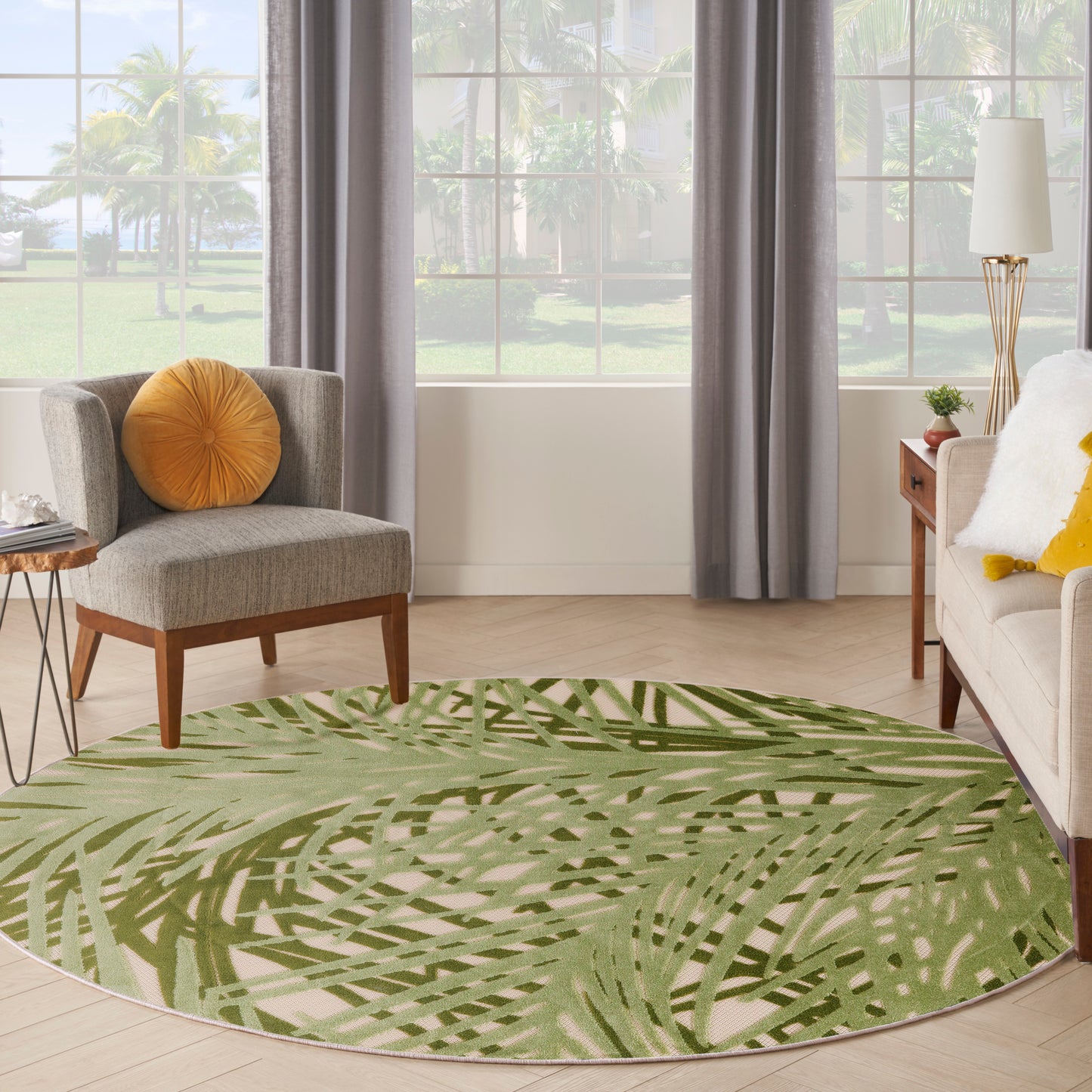 Round green palm-leaf patterned area rug in a modern living room with beige sofa, gray curtains, and wooden furniture.