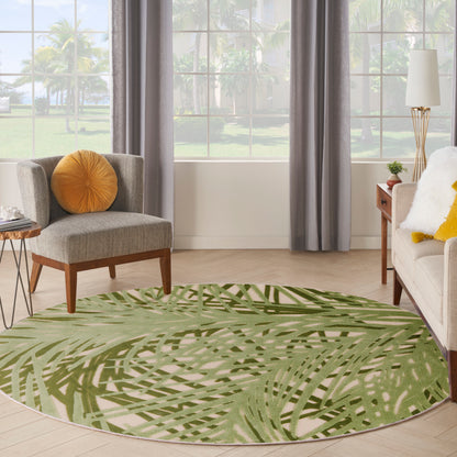 Round green palm-leaf patterned area rug in a modern living room with beige sofa, gray curtains, and wooden furniture.