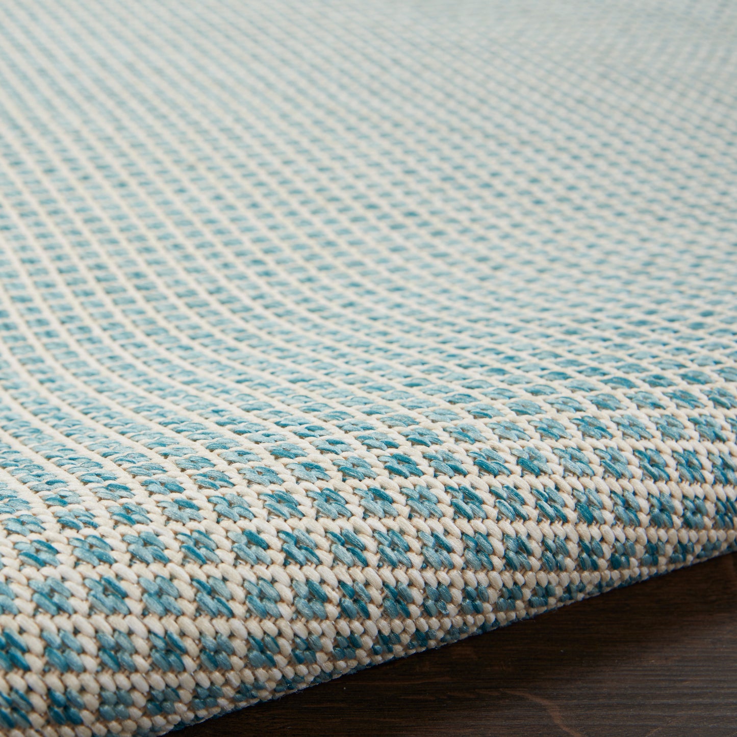 Close-up of a turquoise blue and white woven rug with a small geometric pattern on a dark wood floor.