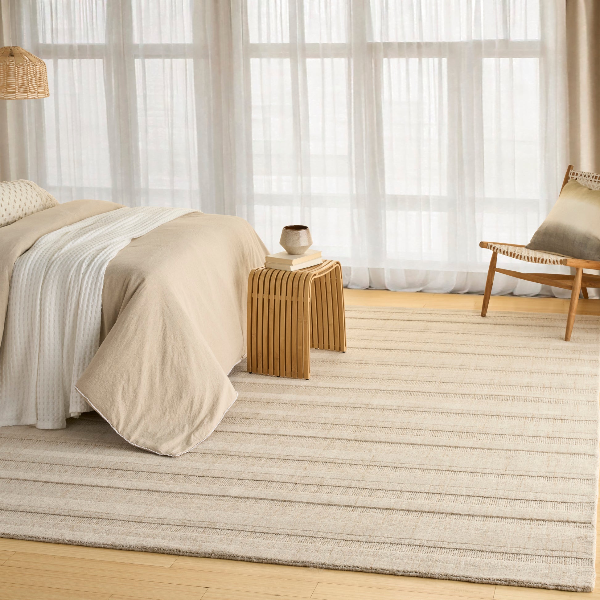 Cream striped rug on light wood floor beside beige bedding and a wooden slat-side table in a bright minimalist bedroom.