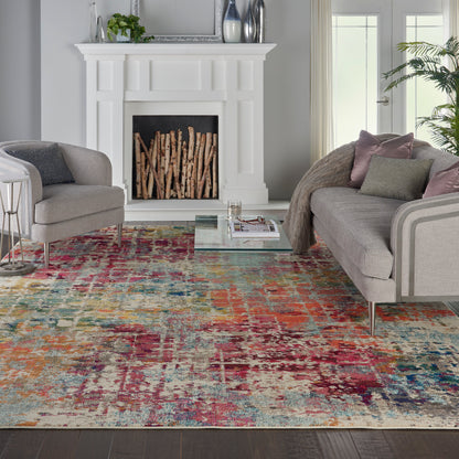 White mantel fireplace with stacked firewood, gray upholstered seating, glass coffee table, & bold multicolor abstract rug.