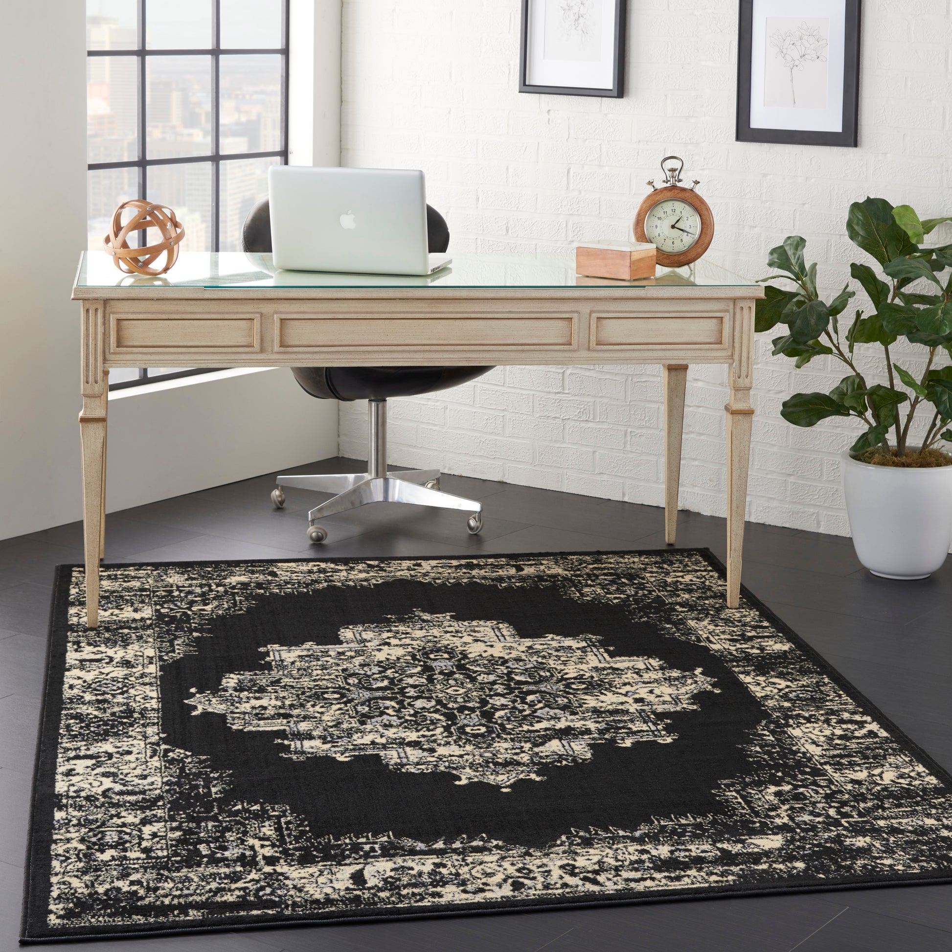 Black and cream oriental rug (6' x 9') on the floor with a beige carved wood desk and glass top, laptop, vintage clock, plant, and a chrome swivel chair.
