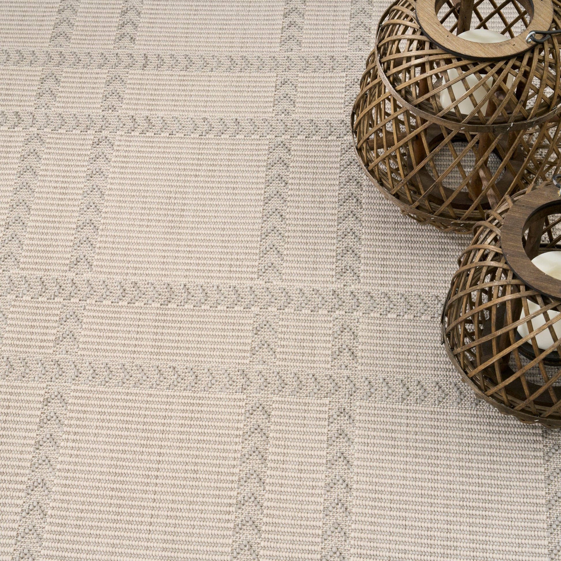 Beige textured woven rug with gray geometric stripes; two brown wicker lanterns on the right.