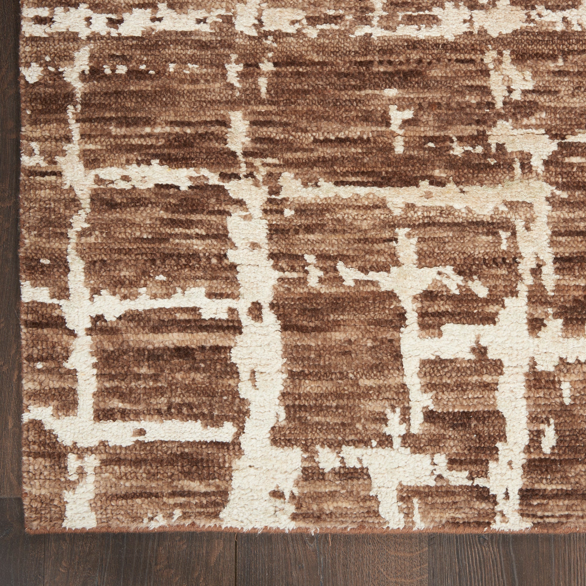Brown area rug with cream geometric pattern and soft plush pile on dark wood floor.
