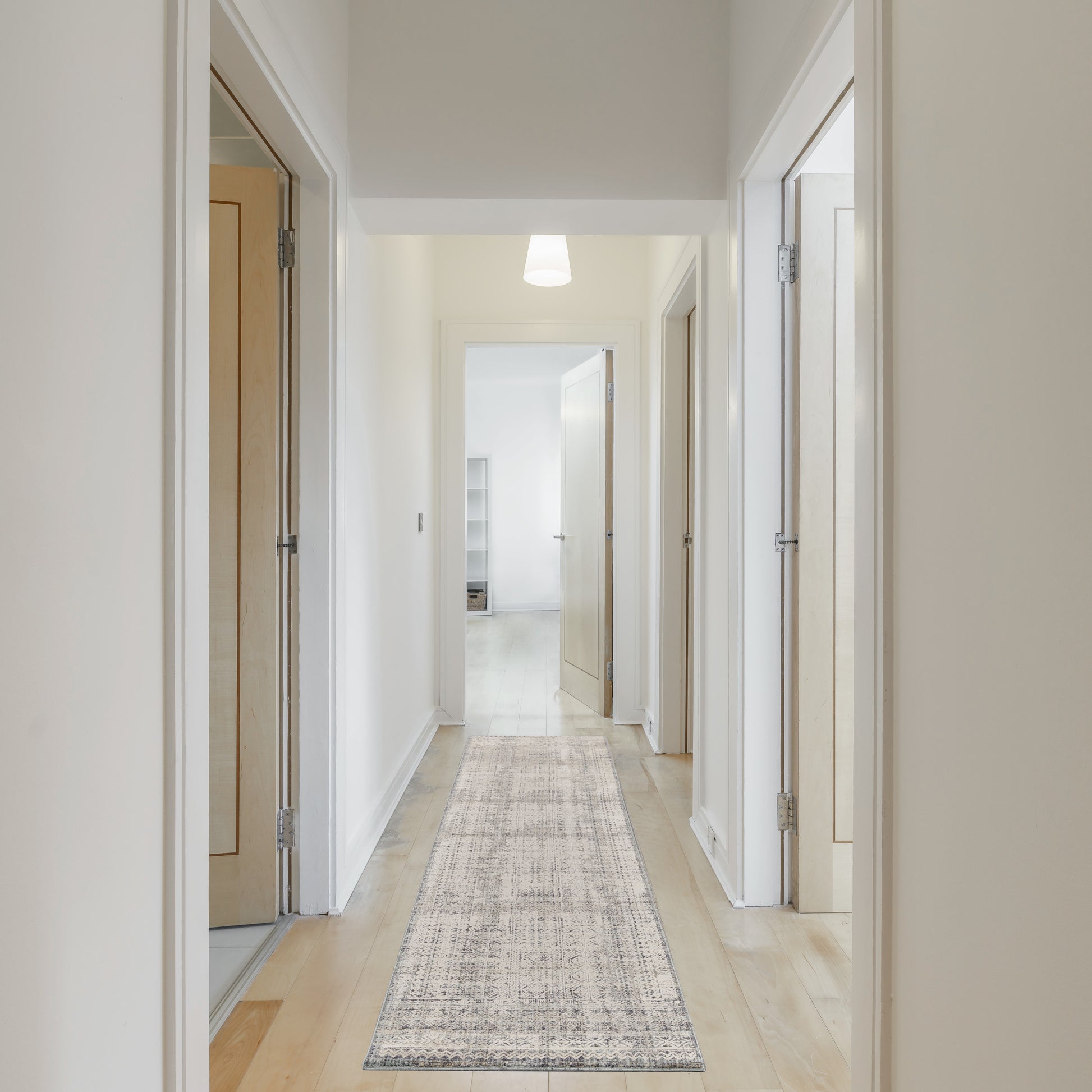 Bright minimalist hallway with white walls, light wood doors on both sides, and a gray patterned runner.