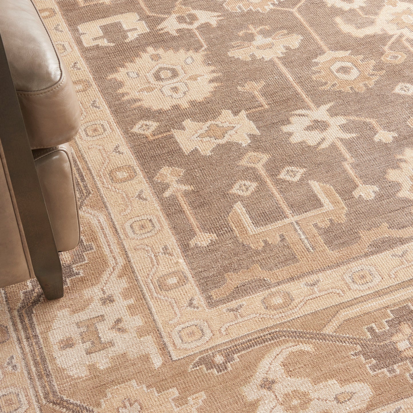 Beige oriental area rug with tan and ivory geometric floral motifs, beside a brown leather sofa.