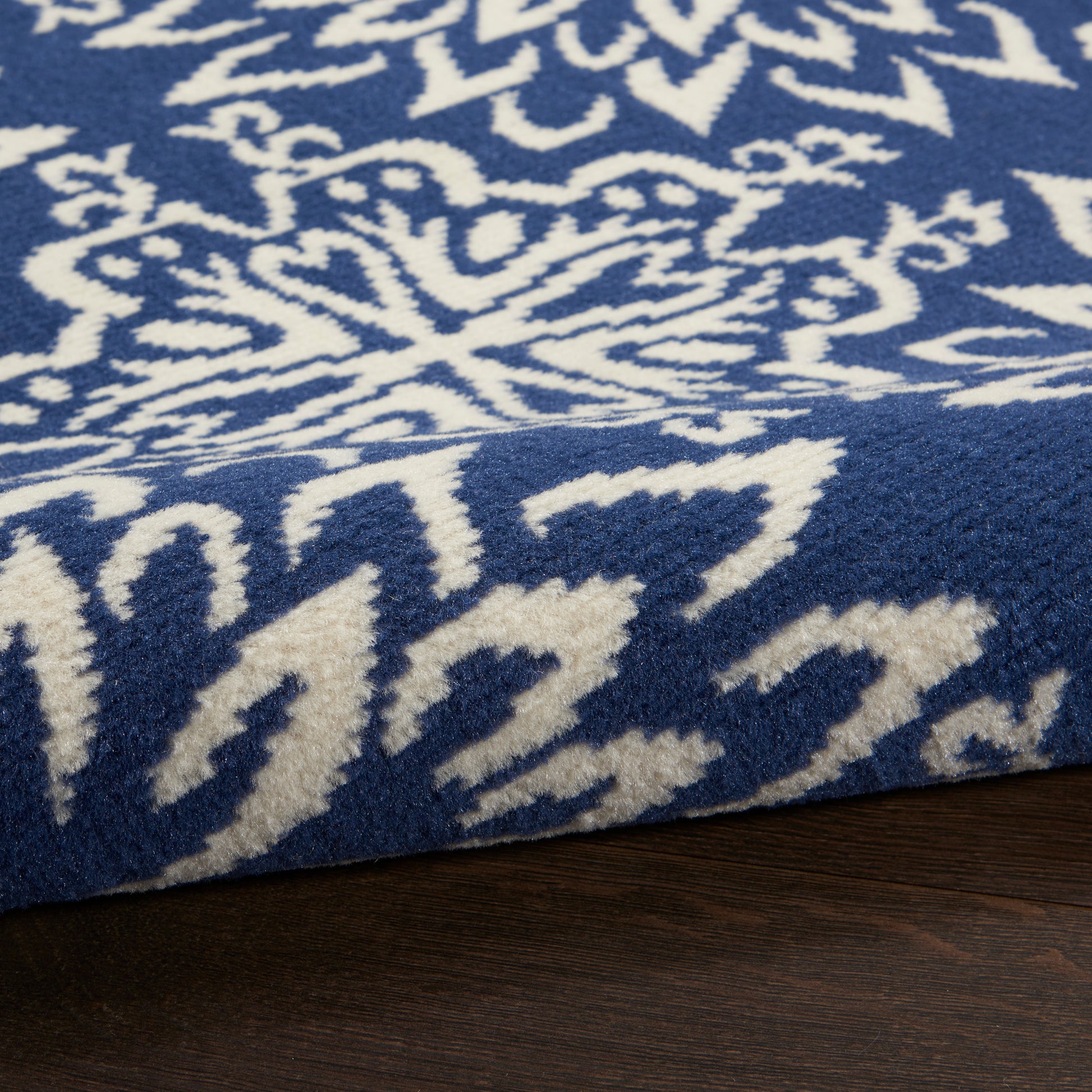 Blue rug & white Nordic snowflake pattern, plush texture, folded corner on dark wood floor.