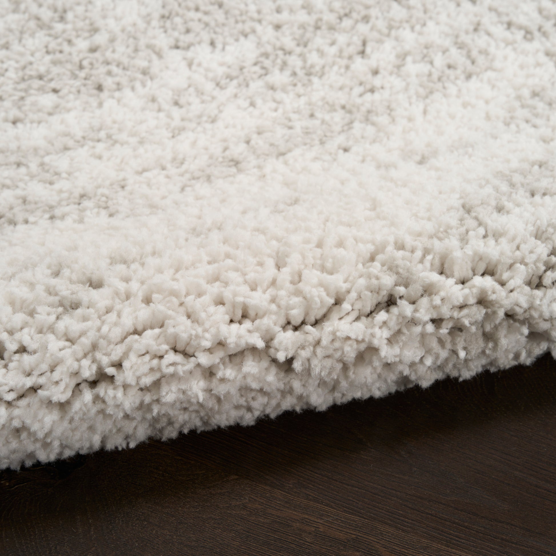 Cream fluffy shag rug with dense plush pile resting on dark wood floor.