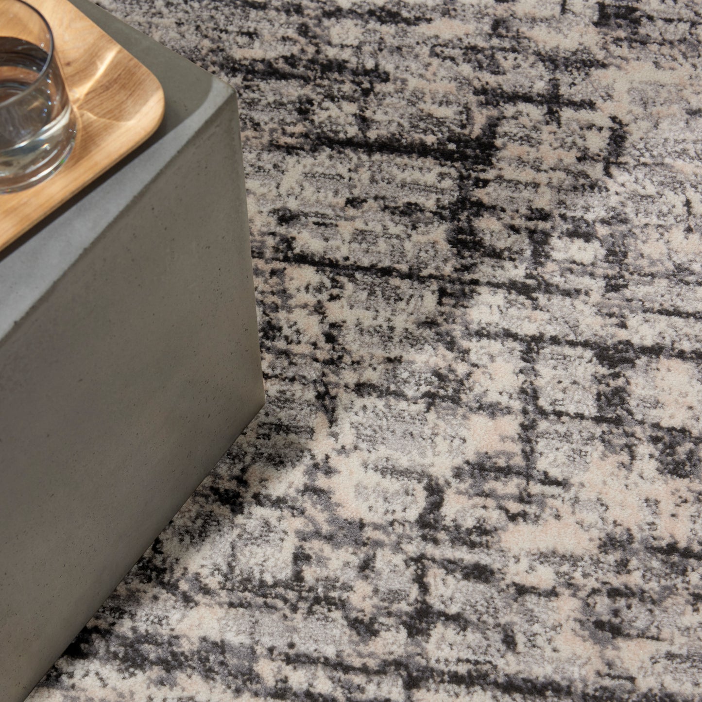 Grey concrete side table with a light wood tray & glass on a black-and-white patterned rug.