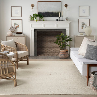 Cozy living room with white mantel fireplace, brick opening, rattan chairs, gray sofa, neutral cushions, beige rug (6' x 8'), art.