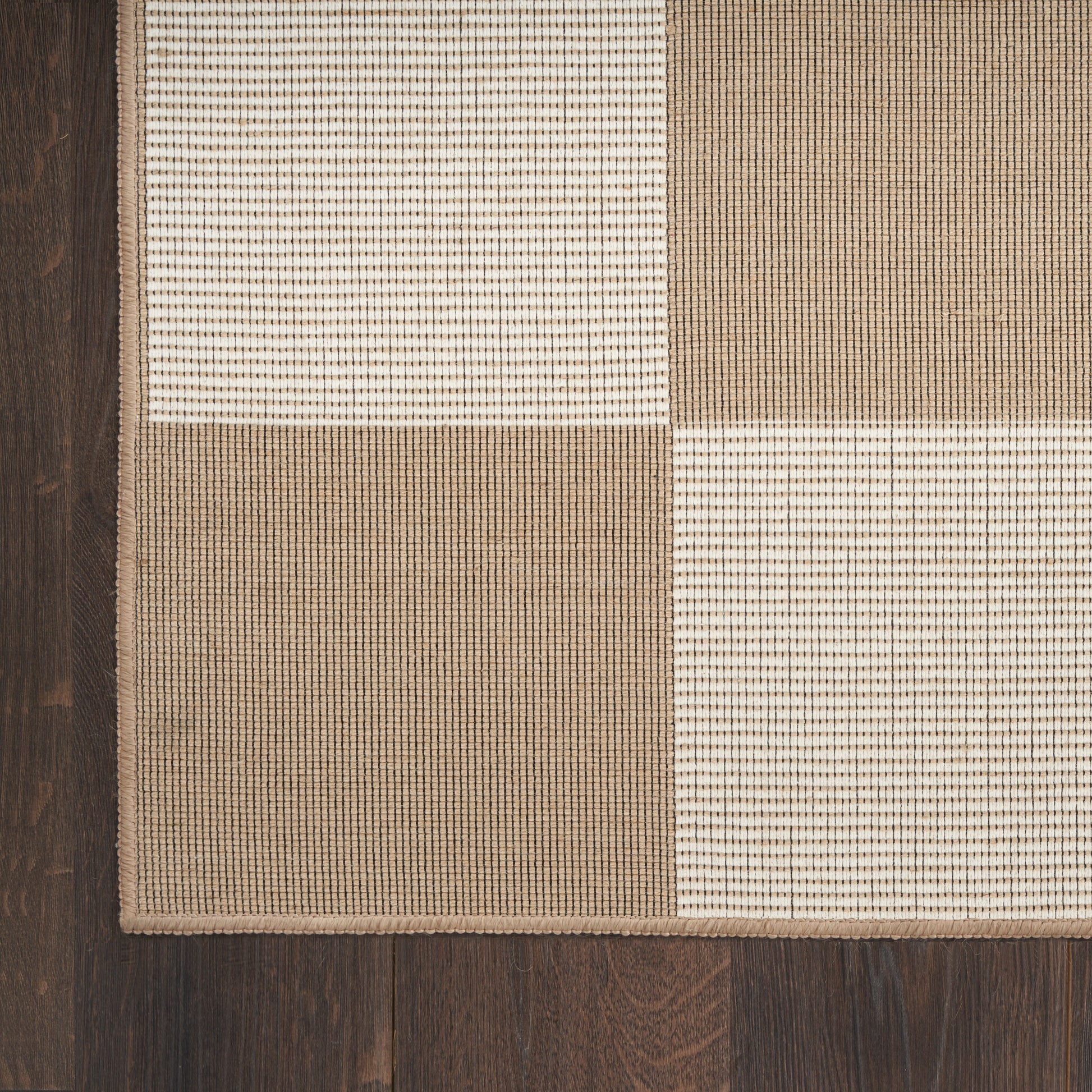 Beige, ivory and tan patchwork rug with woven square textures on dark wood floor.