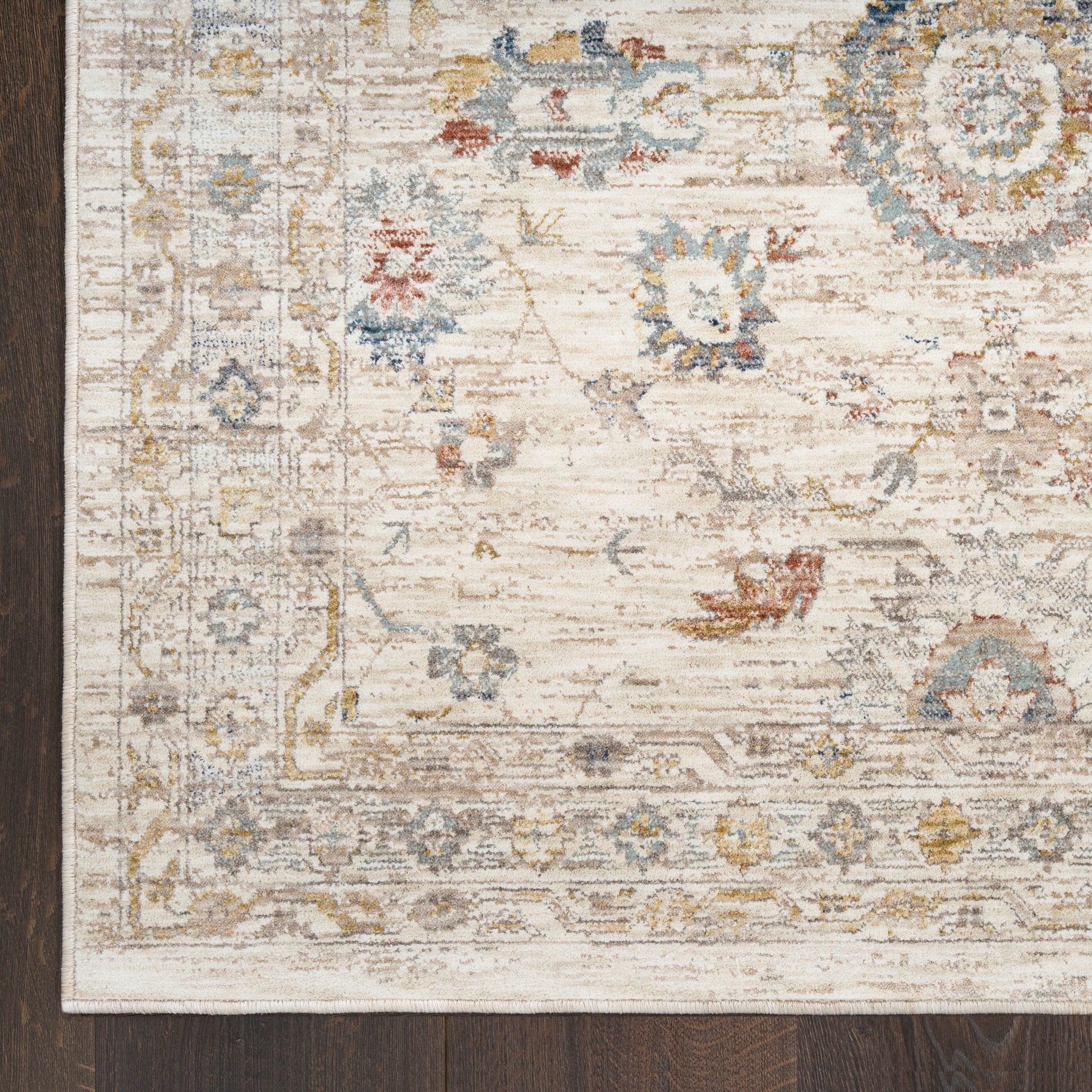Cream distressed rug with blue, yellow and pink floral motifs and decorative border on dark wood floor.
