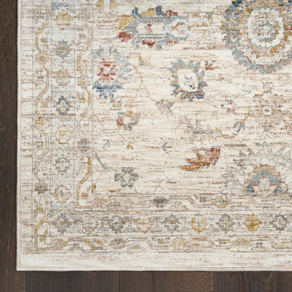 Cream distressed rug with blue, yellow and pink floral motifs and decorative border on dark wood floor.