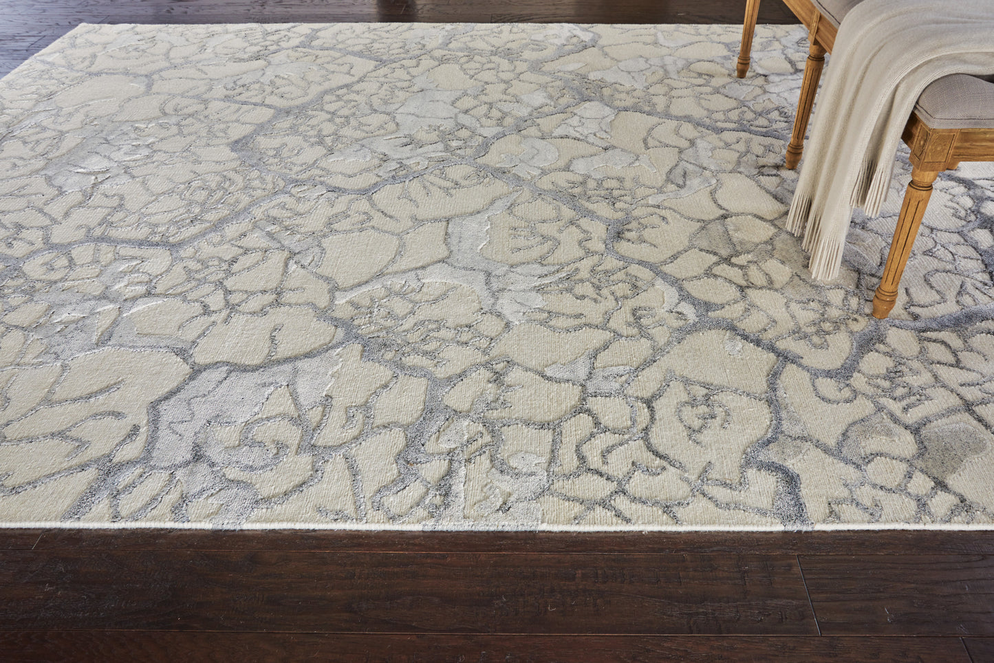 Ivory-gray cracked-stone area rug on dark hardwood floor, with a wooden chair and cream throw.