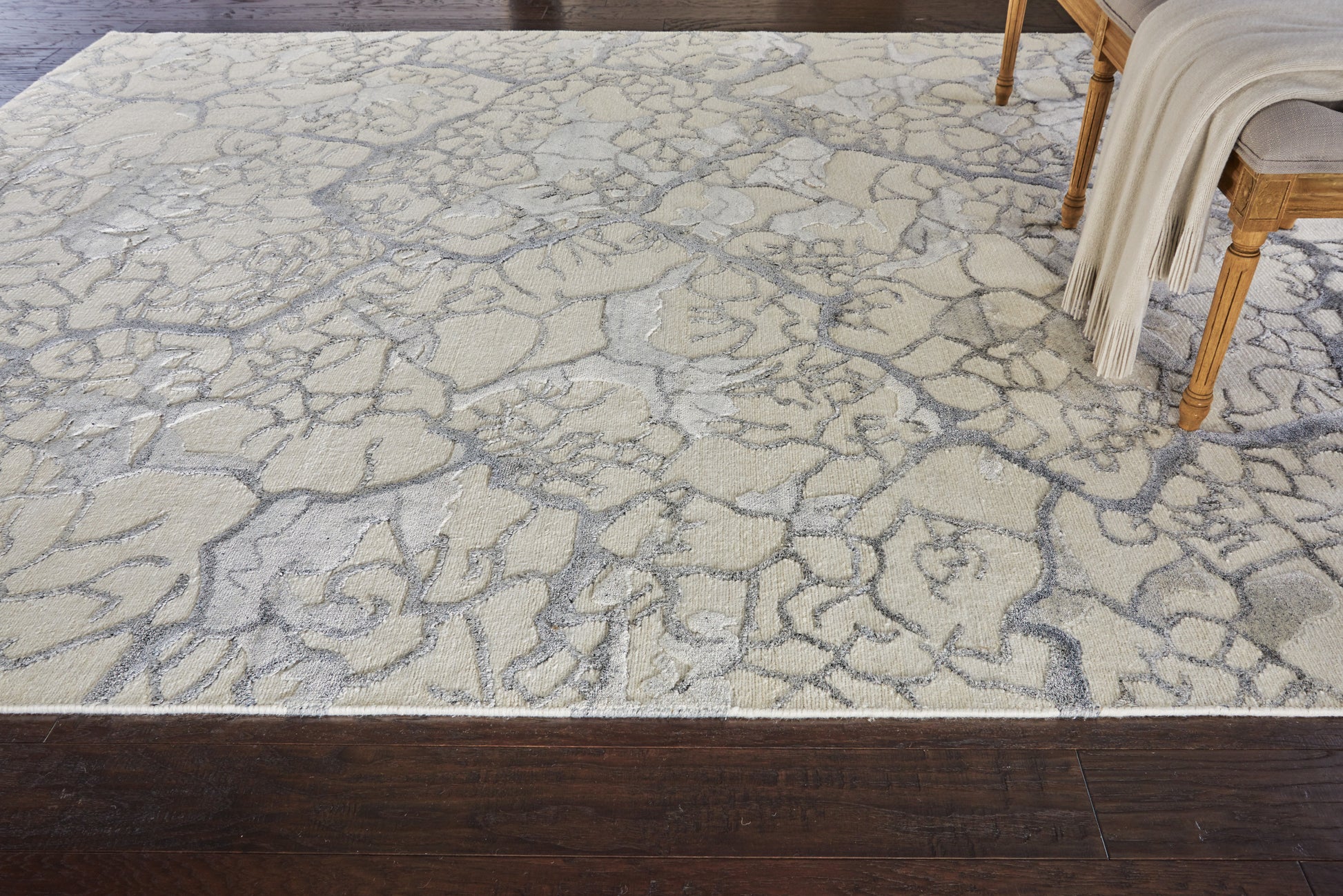 Ivory-gray cracked-stone area rug on dark hardwood floor, with a wooden chair and cream throw.