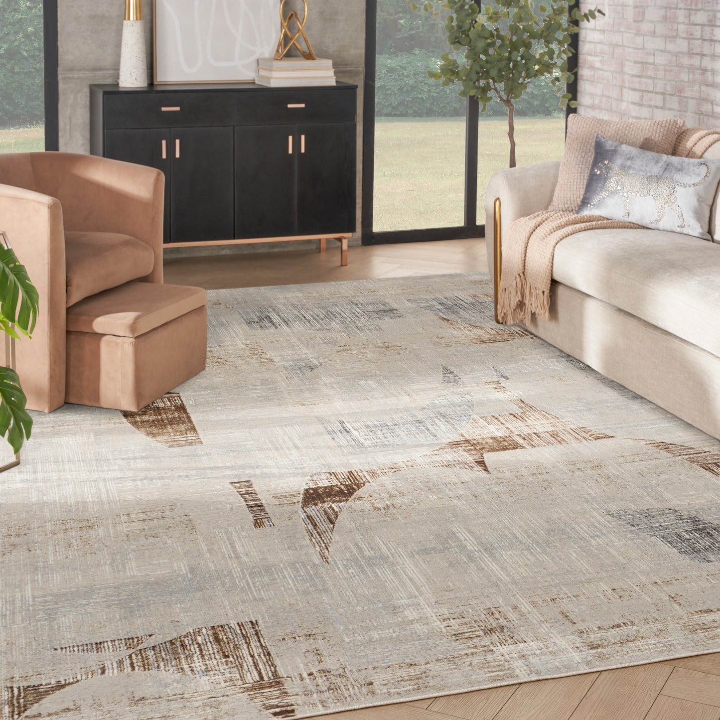 Neutral abstract area rug with beige, gray, and brown patches, in a contemporary living room with tan chair and beige sofa.