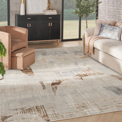 Neutral abstract area rug with beige, gray, and brown patches, in a contemporary living room with tan chair and beige sofa.