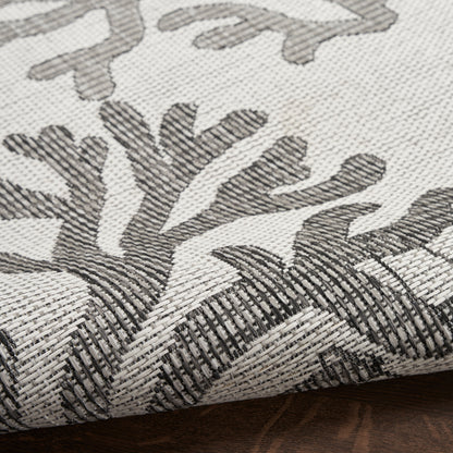 Beige woven rug with dark gray botanical leaf pattern and a rolled edge; textured diagonal weave.