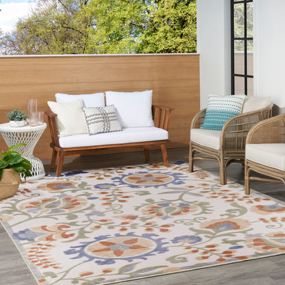 Outdoor patio with a wood-framed sofa, wicker chairs, white cushions, and a colorful floral rug; potted plant and glass door.