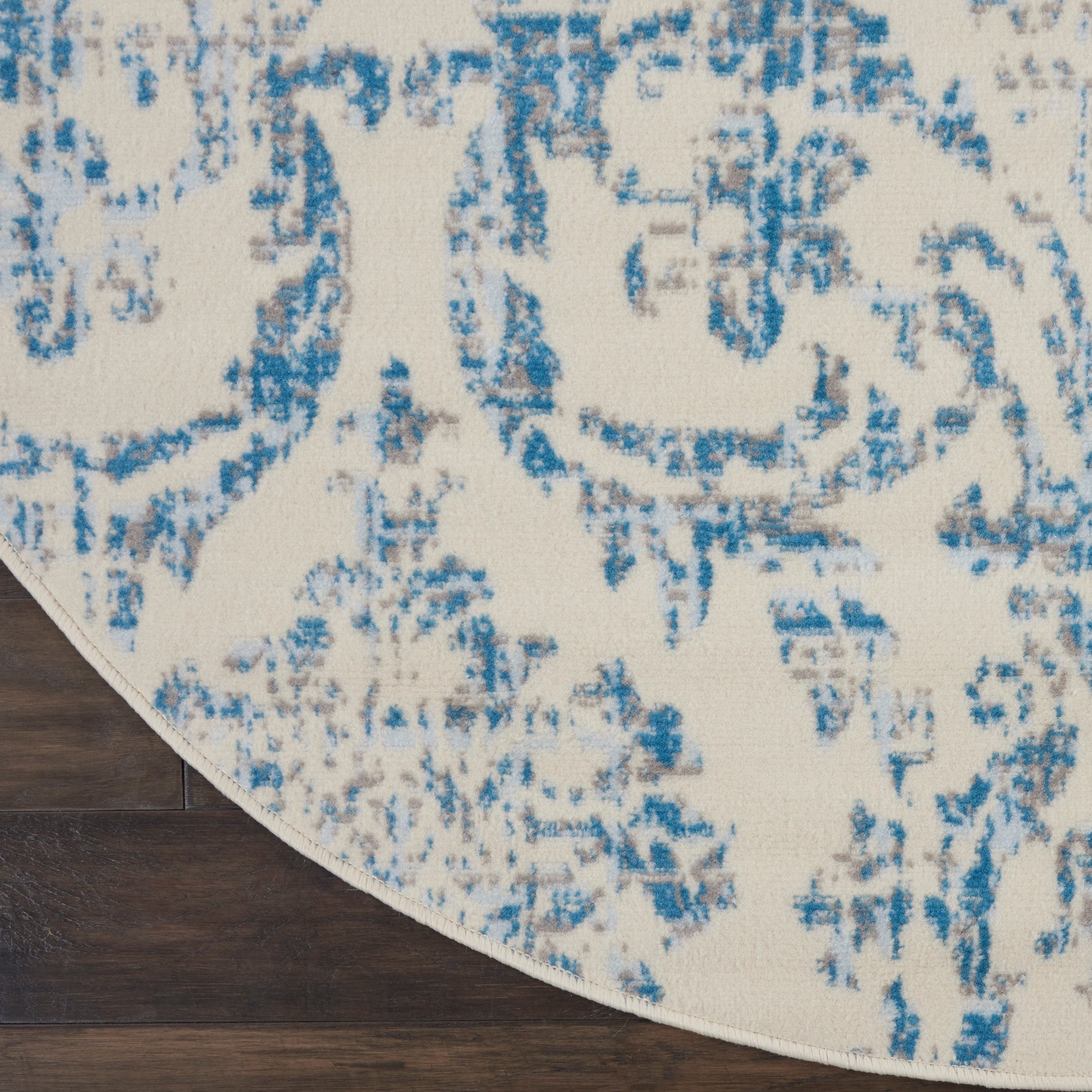 Round cream rug with blue distressed floral pattern; soft low-pile texture for living room decor.