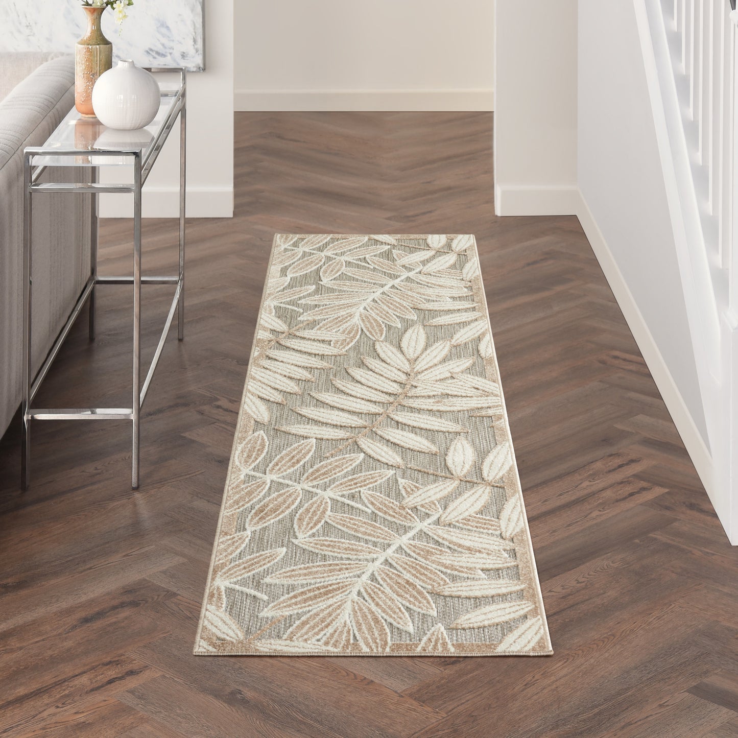 Beige botanical leaf-pattern runner rug in entryway, cream and tan tones on dark wood floor with chrome console table.