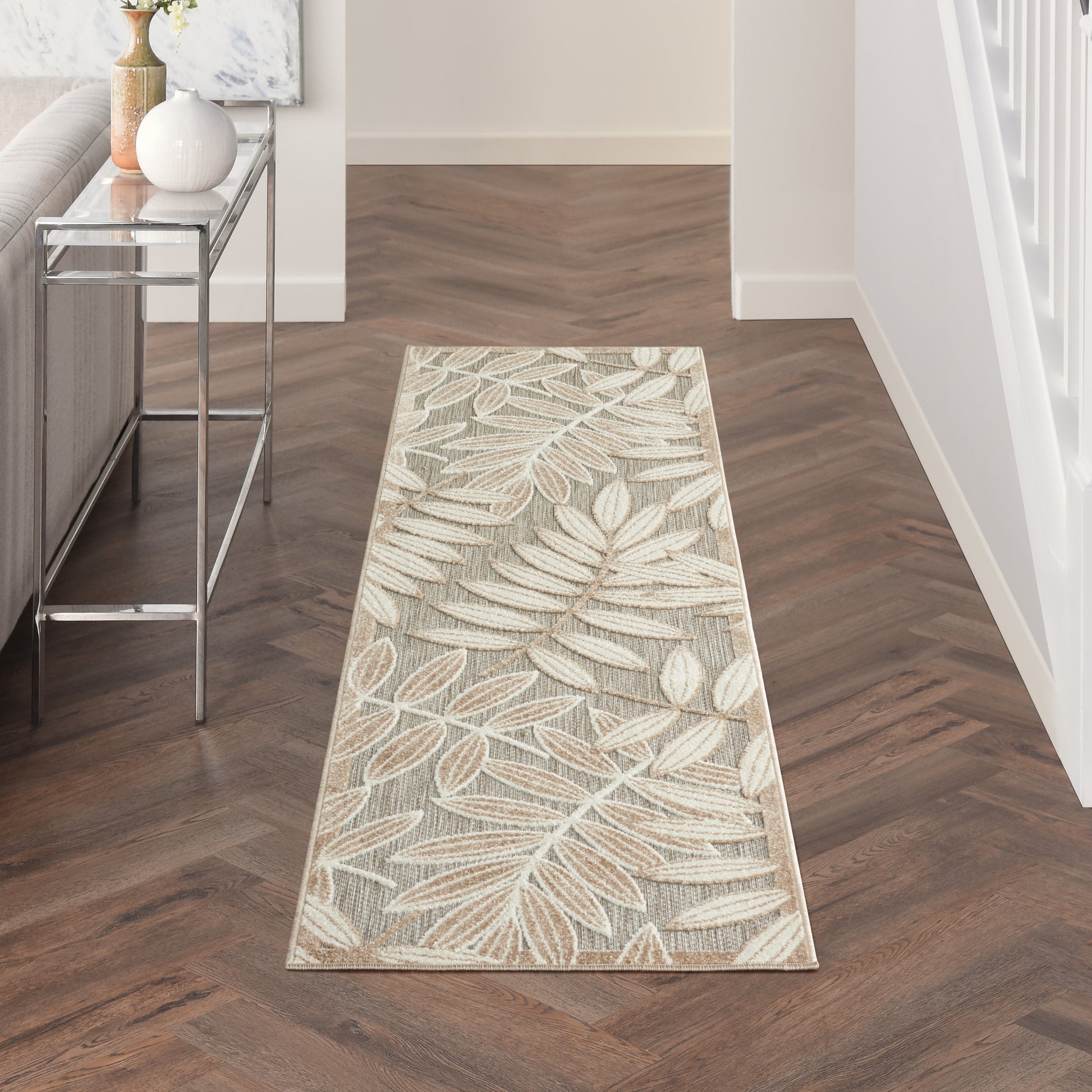 Beige botanical leaf-pattern runner rug in entryway, cream and tan tones on dark wood floor with chrome console table.