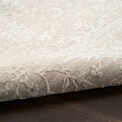 Beige damask patterned area rug with soft plush pile and ivory floral motif, folded edge on dark wood floor.