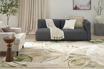 Modern living room with dark gray sofa, cream throw, beige rug with green leaf pattern, white armchair and plants.