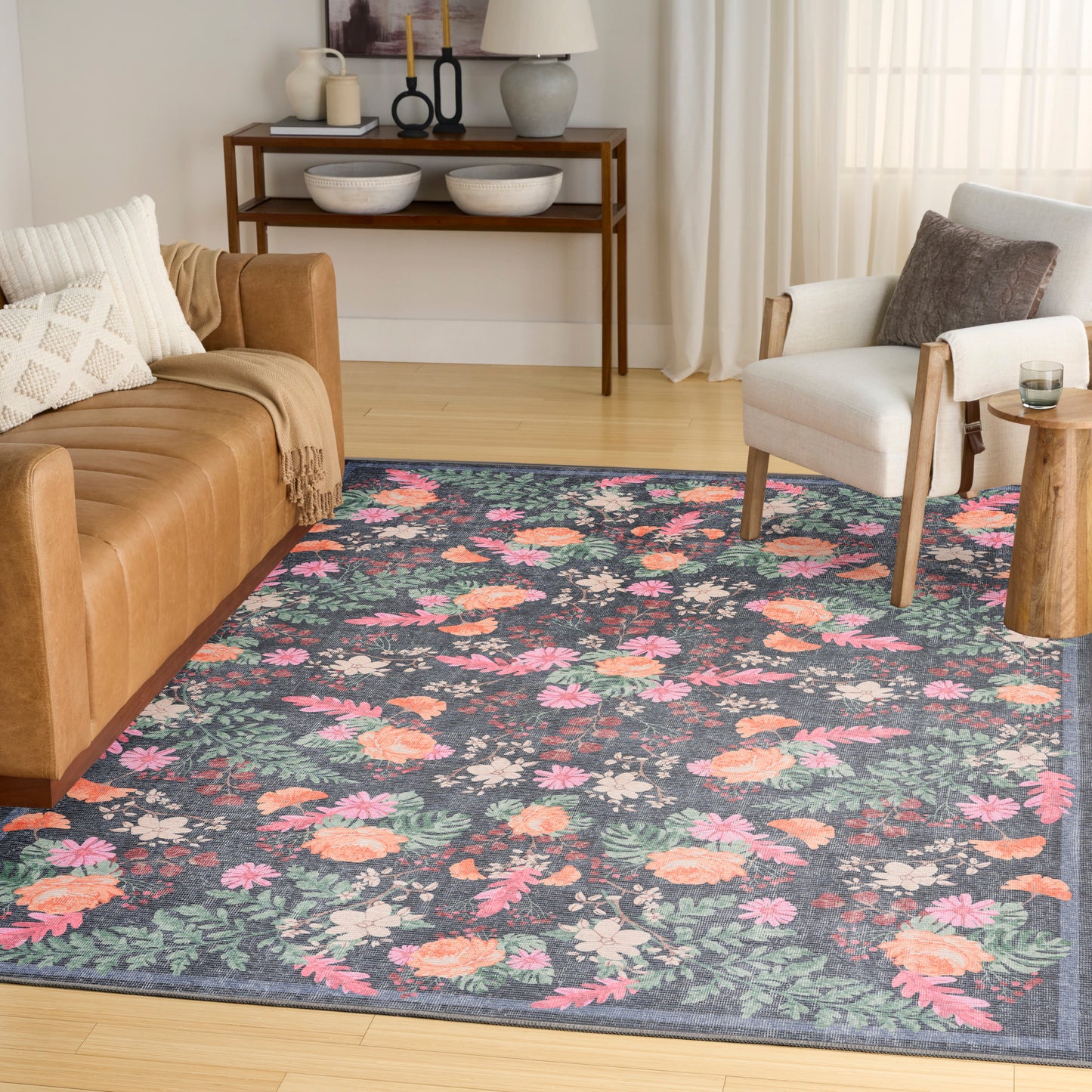 Living room with navy floral rug in pink and peach blossoms, tan leather sofa, white armchair, and wooden console table.