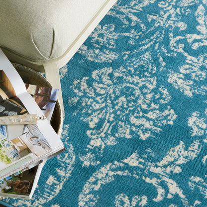 Turquoise blue rug with white damask pattern; beige upholstered chair and scattered magazines with a bracelet.