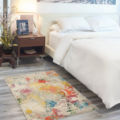 White bed with plush pillows, dark wood nightstand, lamp, framed photo; multicolor abstract rug on gray wood floor.