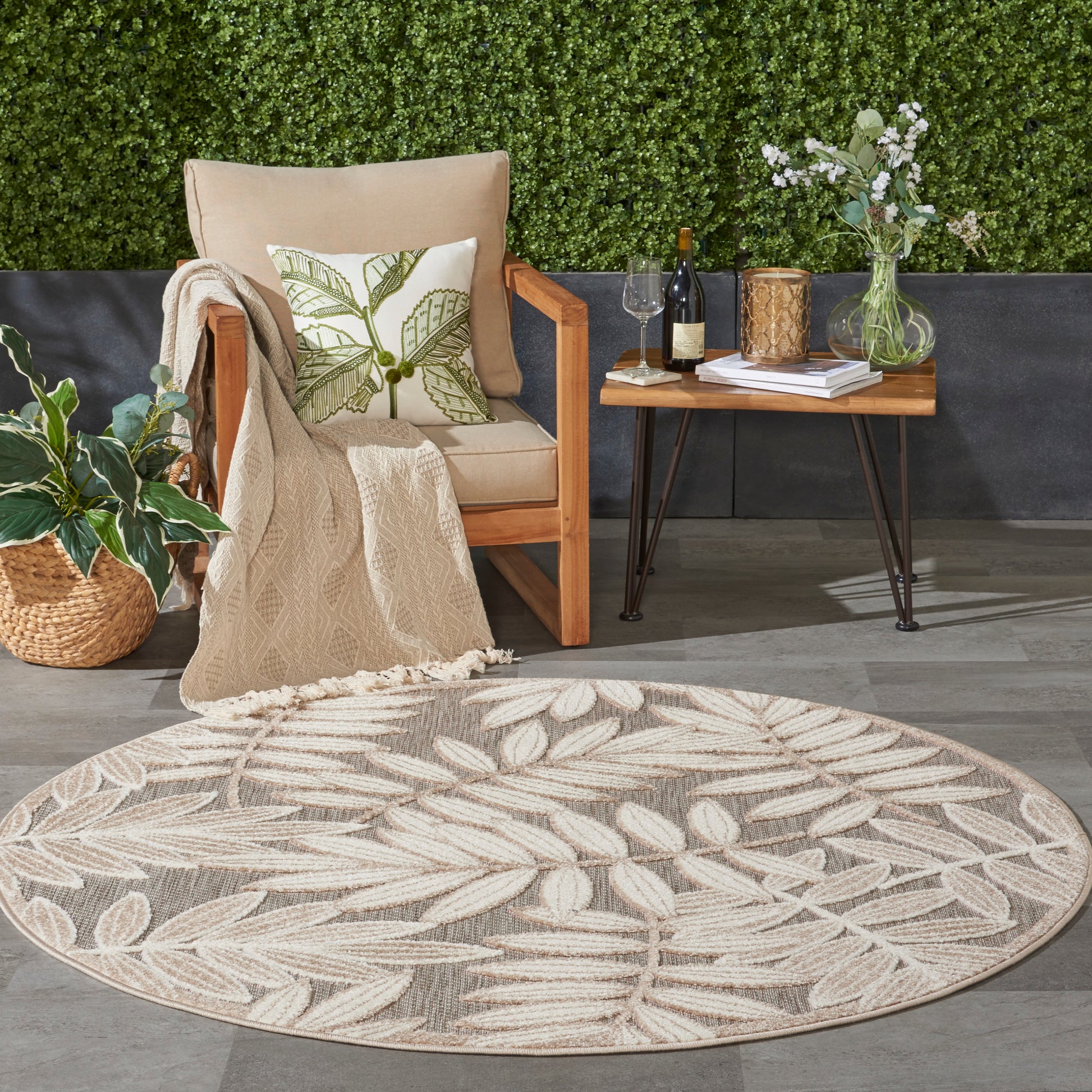 Round beige outdoor rug with cream leaf pattern beside a wooden chair and side table with wine and flowers