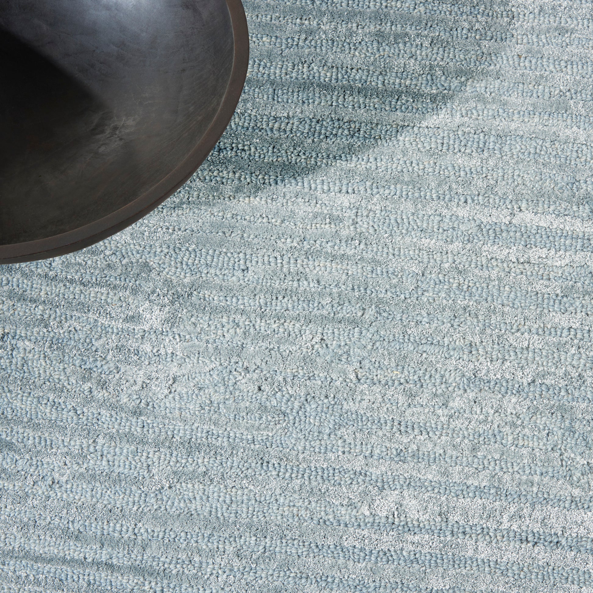 Partial view of a light blue textured rug with a subtle geometric pattern.