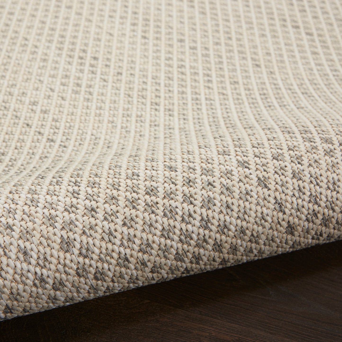 Beige natural-fiber woven rug with vertical ribbed texture and subtle border on dark wooden floor.