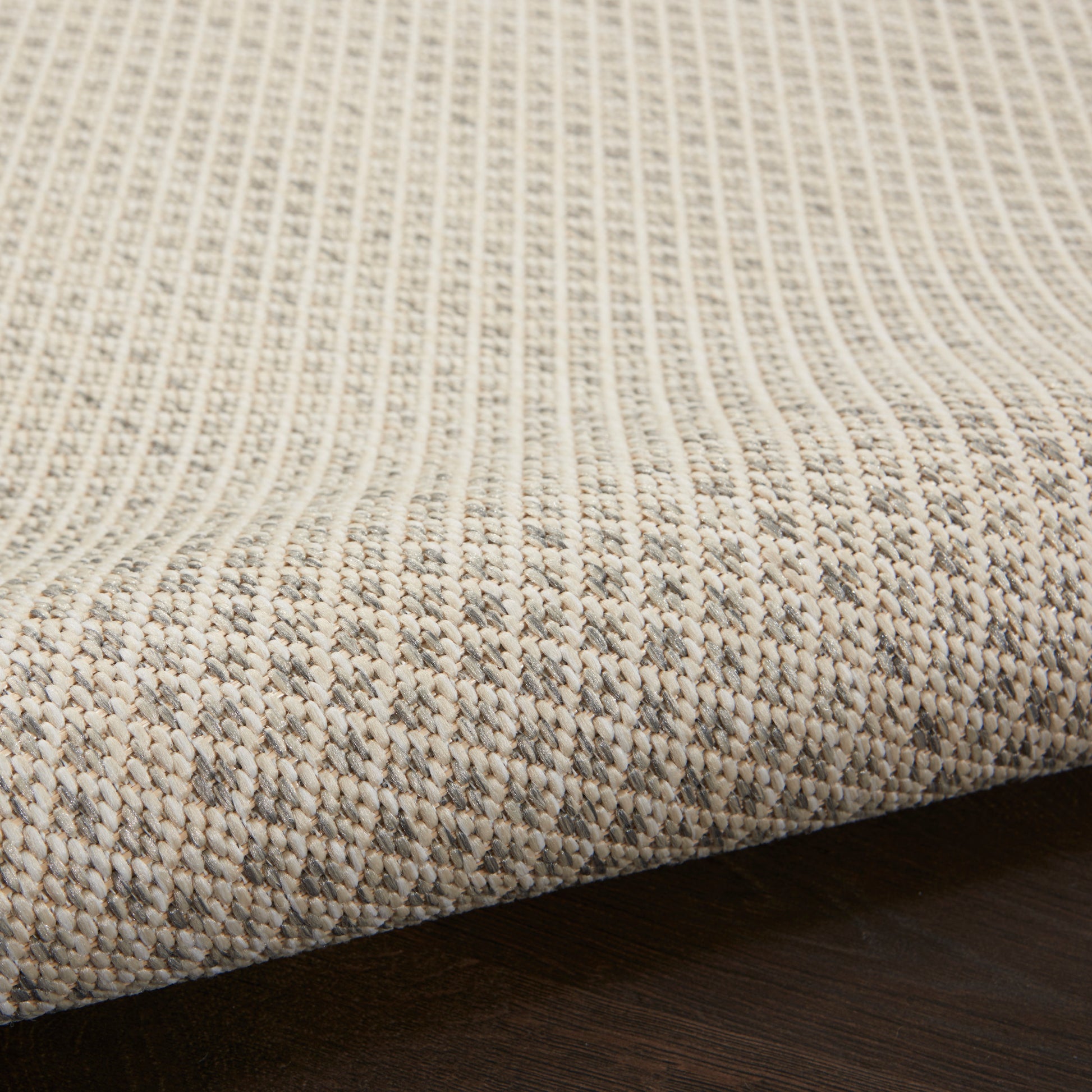 Beige natural-fiber woven rug with vertical ribbed texture and subtle border on dark wooden floor.