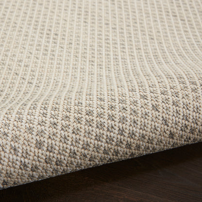 Beige natural-fiber woven rug with vertical ribbed texture and subtle border on dark wooden floor.