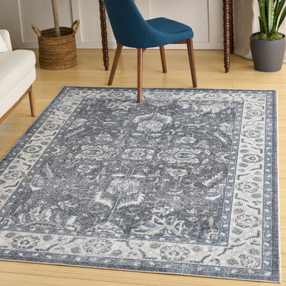 Blue-gray patterned area rug with floral medallion border on light wood floor; modern living room with blue upholstered chair.