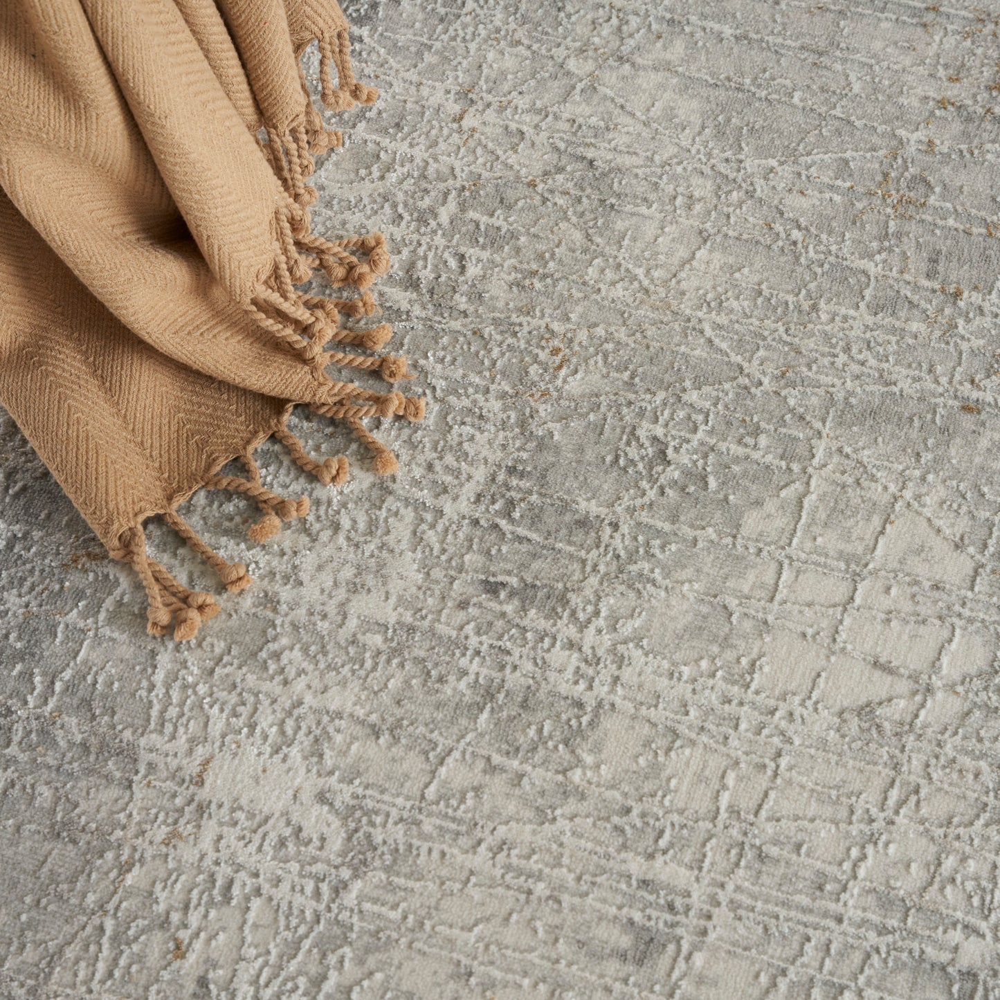Beige woven rug with fringed tassels on a textured gray surface.