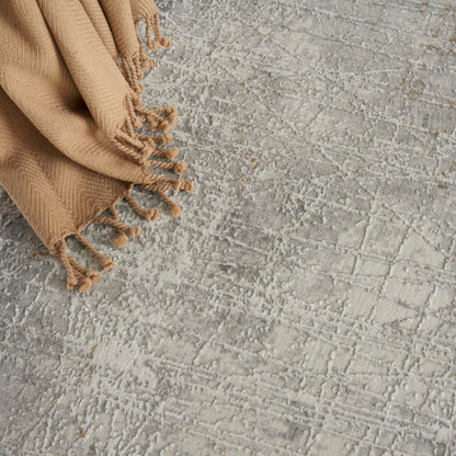 Beige woven rug with fringed tassels on a textured gray surface.