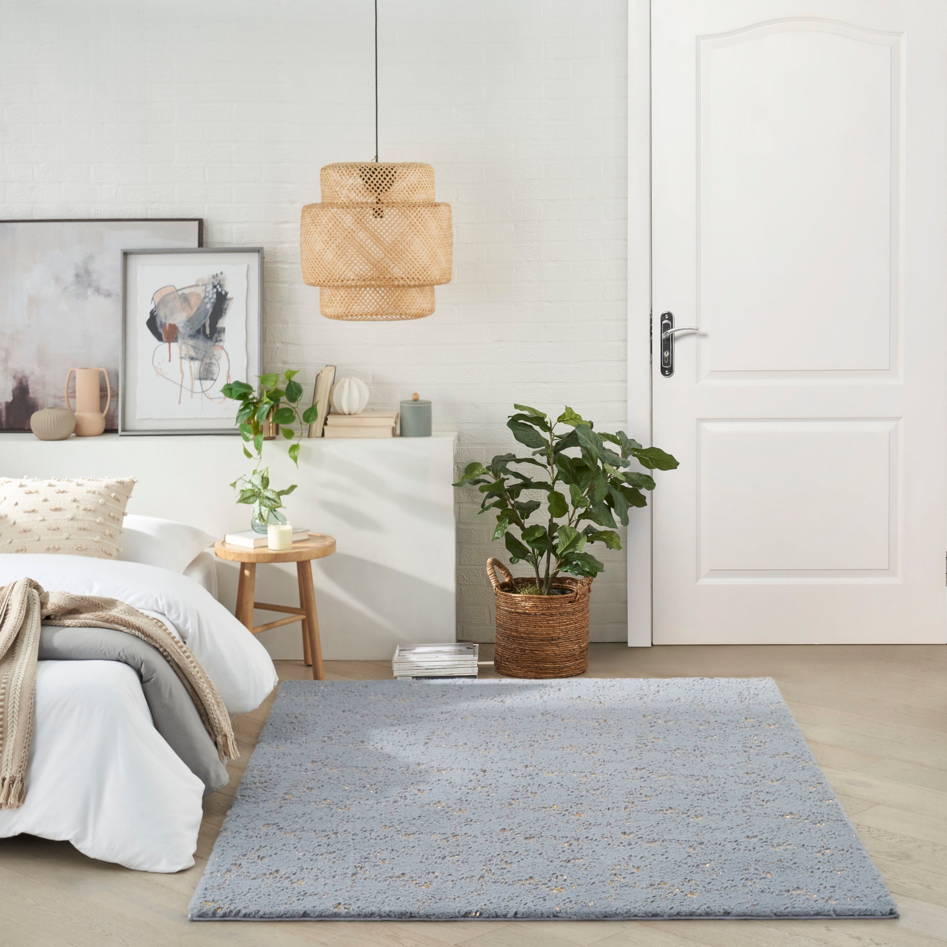 Modern bedroom with white walls, wicker pendant light, gray-blue rug, potted plant, wooden side table & framed art.