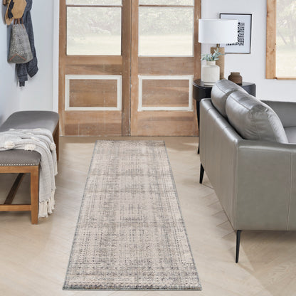 Gray patterned runner rug on light wood floor between a gray sofa and bench in a bright entryway with wooden doors.