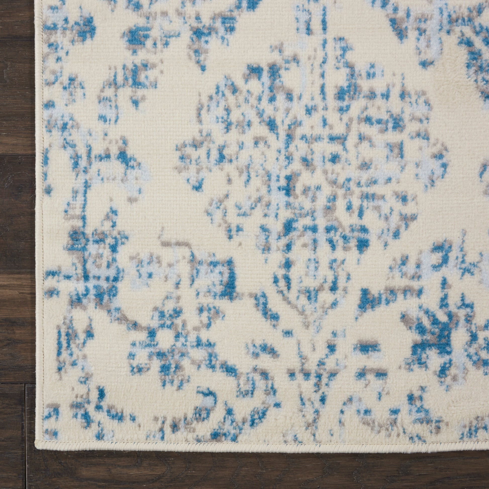 Ivory rug with blue distressed floral damask pattern; rectangular, on dark wooden floor.