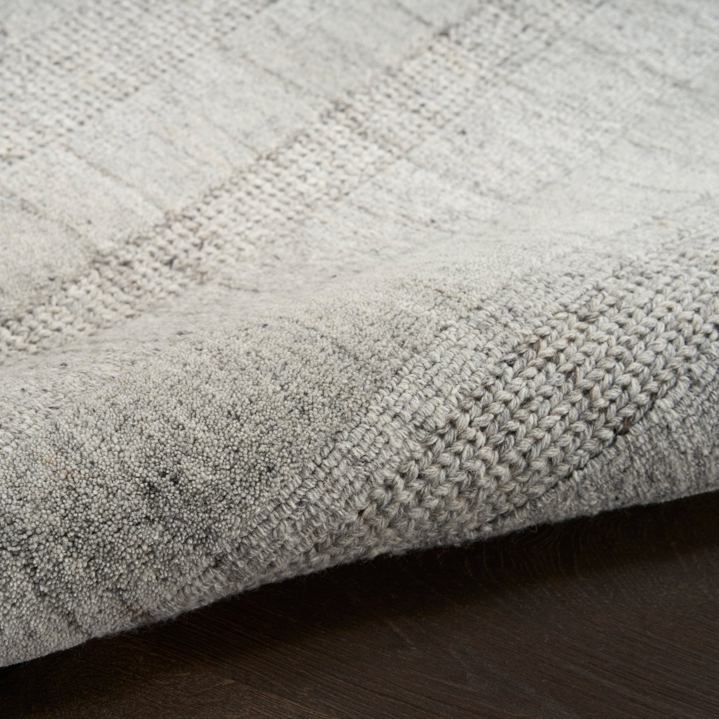 Grey textured area rug with subtle geometric pattern and plush pile on dark wood floor.