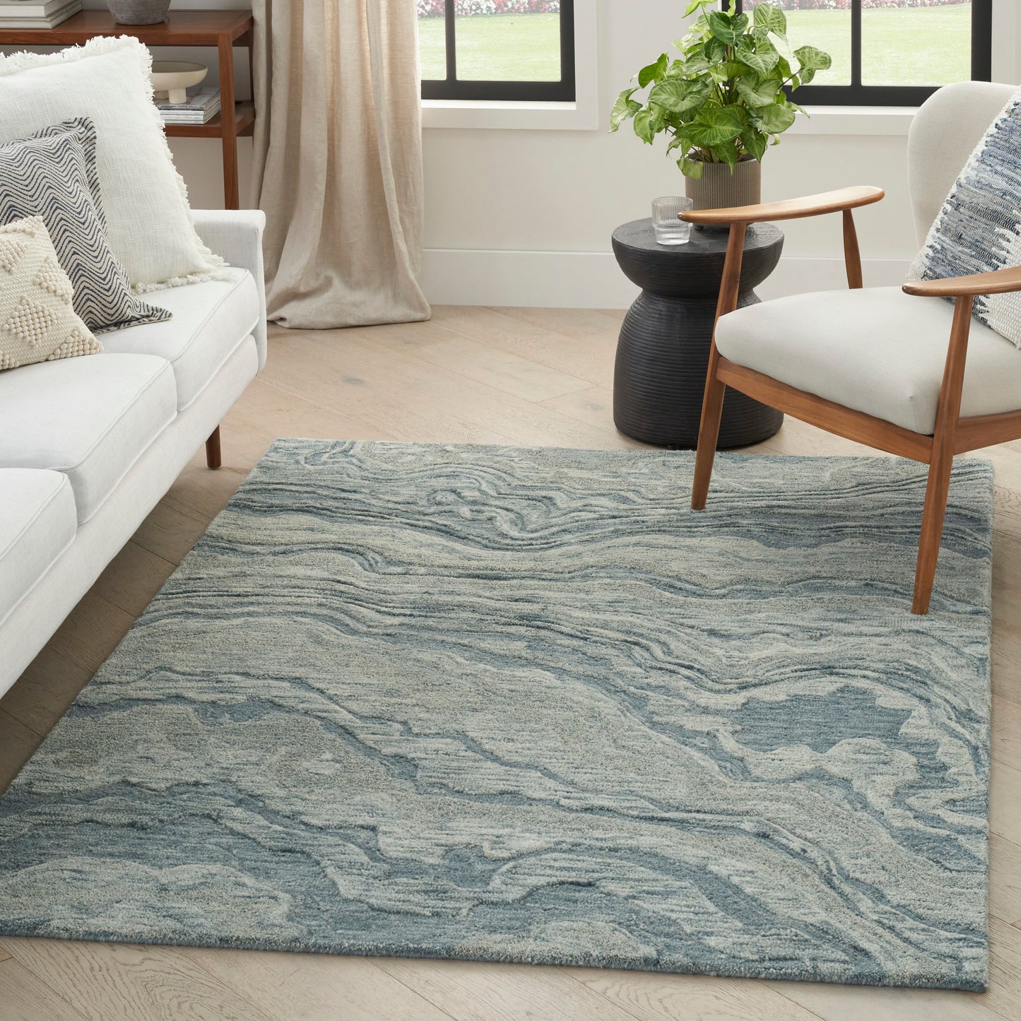 Blue-gray marbled area rug in a bright living room with a white sofa, wooden armchair, and a green plant.