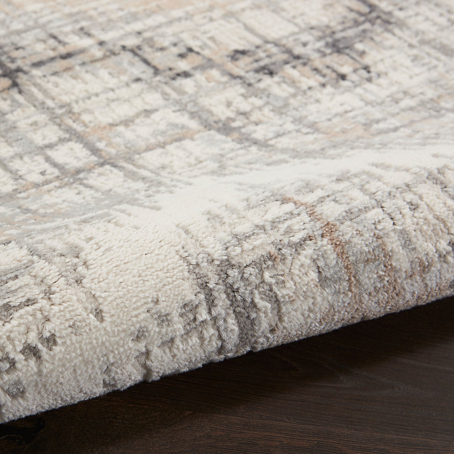 Close-up of a cream, beige and gray geometric area rug with a soft tufted pile on dark wooden floor.